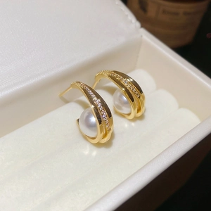 Close-up of gold C-shaped earrings with white round pearl and pavé cubic zirconia