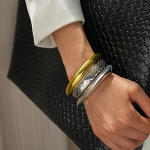 Close-up of stacked gold and silver textured geometric metal bangles on a model's wrist