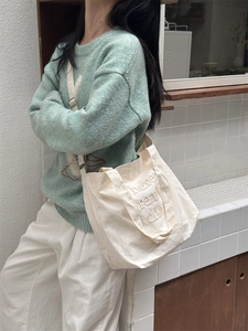 Detail of off-white canvas tote bag with embroidery on casual knit sweater outfit