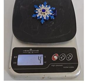 Detail shot of a 4g snowflake rhinestone hair clip on a digital scale for weight display