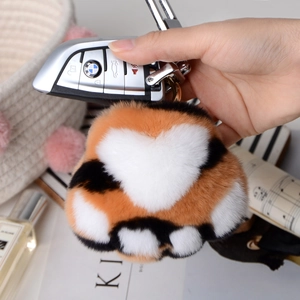 Detail of soft tricolor plush cat paw keychain hanging on a luxury car key