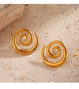 Detailed view of gold spiral earrings with clear gemstone on a natural textured surface