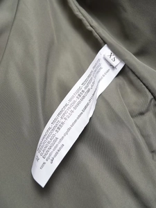 Dettaglio dell'etichetta con 100% cotone e taglia XS sulla giacca di colore verde