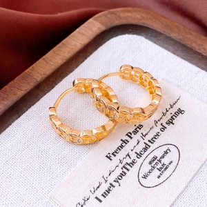 Macro detail of 18K gold plated hoop earrings with white zircon on elegant texture background