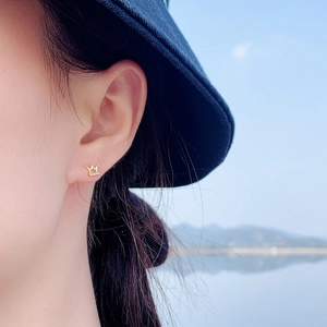 Elegant gold crown stud earrings with diamonds worn by model in a natural setting