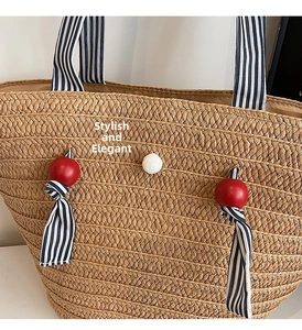 Detail view of woven straw beach tote bag with blue striped fabric handles and red wooden beads