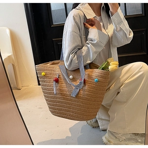 Detail of woven straw tote bag with colorful pom-poms and striped handles for beach