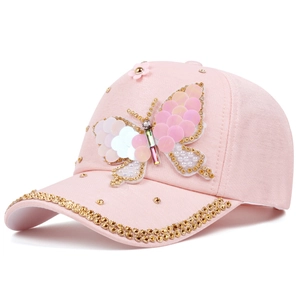 Détail d'une casquette rose avec papillon en paillettes, fleur et perles dorées bordées
