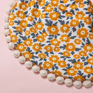 Détail de bavoir bébé à imprimé marguerites avec bordure pompon blanc sur fond rose