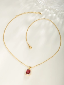 Detail of gold necklace featuring square red gemstone pendant with zircon border