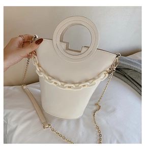Detail of white bucket bag with circular handle, chunky chain decor and metal strap