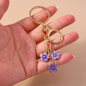 Golden cherry blossom keychain with purple enamel flowers held against pink background