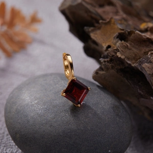 Macro detail of gold-plated silver pendant featuring a square-cut deep red gemstone