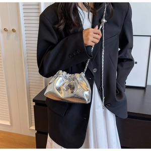 Detail of silver pleated bucket bag with metallic finish and elegant chain strap on shoulder