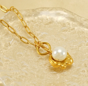 Dettaglio del ciondolo di perla bianca su una catena a maglie grosse dorate