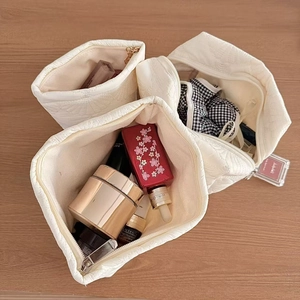 Three-piece white floral quilted makeup bags for travel storage on wooden surface