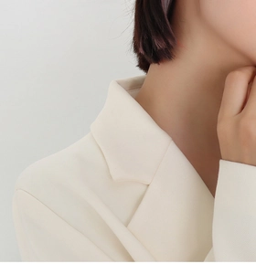 Detailed close-up of notched lapel and textured woven fabric on an ivory blazer