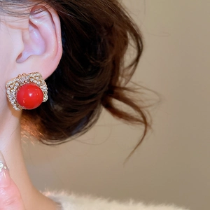 Detail of red spherical bead earring with gold base and zircon inlay worn on ear