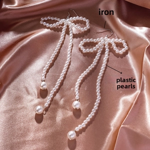 Detail of bow earrings with iron hooks and plastic pearls on silk fabric