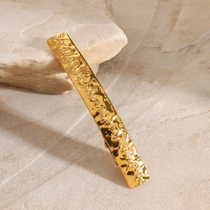 Close-up of golden stainless steel hair clip with embossed leaf pattern on natural stone