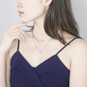 Detailed view of layered heart necklace featuring pearls and silver metallic chain on neck