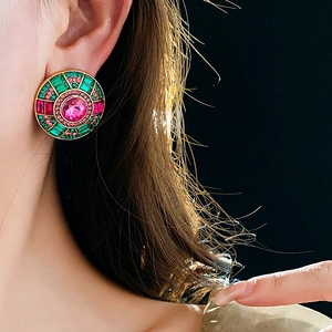 Macro detail of vintage round gold earrings with pink and green rhinestones worn by model
