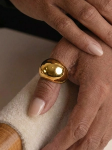 Close-up of minimalist chunky golden dome ring worn on finger with warm aesthetic lighting