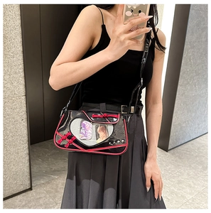 Detail of black patent leather bag featuring a heart-shaped clear window and red knot accent