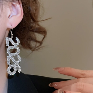 Dettaglio di orecchini a nappa scintillanti con strass e design creativo del numero 2023
