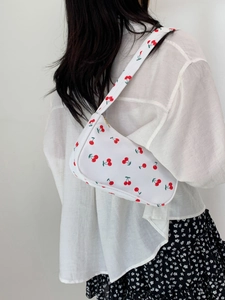 Close-up of white nylon shoulder bag featuring vibrant red cherry patterns and gold zipper