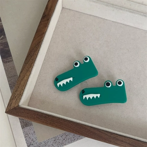 Detail of two green acrylic crocodile hair clips on a beige jewelry display tray