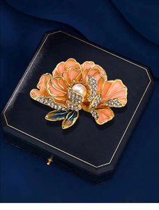 Macro shot of pink enamel peony brooch with pearl center and crystals on blue box