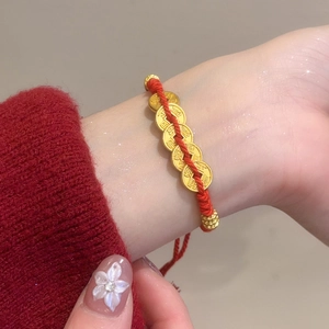 Close-up of a red woven bracelet with five golden coins on a woman's wrist