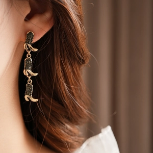 Detail of gold boot tassel earrings with dark rhinestones worn by a model in close-up
