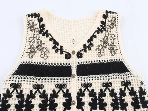 Detail of crochet knit vest featuring floral embroidery, wood buttons, and tassel hemline