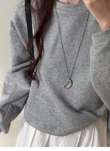 Silver bead chain necklace with abstract curved pendant worn on a grey sweater