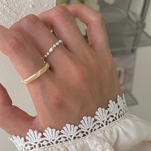 Macro view of stacked silver beaded chain ring and beige marble resin ring on finger