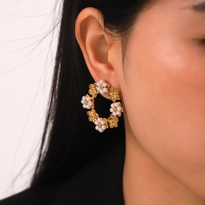 Gros plan sur des boucles d'oreilles couronne de fleurs dorées et perles blanches
