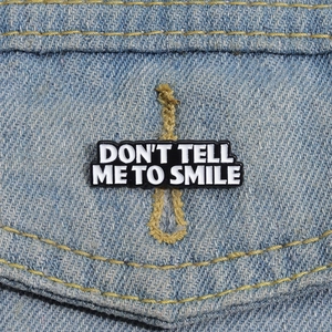 Close-up of Don't Tell Me To Smile enamel pin on a denim jacket pocket