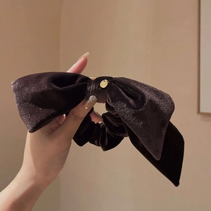 Close-up of velvet bow hair scrunchie in dark brown with a small golden charm detail