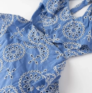 Detailed macro view of white floral eyelet embroidery and ruffles on a blue midi dress