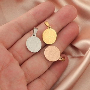 Three Saint Benedict medals in silver, gold, and rose gold on pink silk background