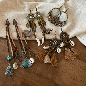 Detailed view of bohemian tassel earrings with turquoise beads and feathers on wood background