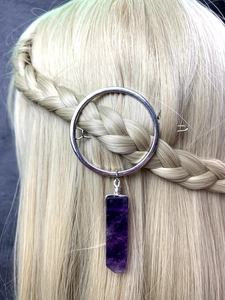 Close-up of a silver round hair clip with a purple crystal pendant on blonde braided hair