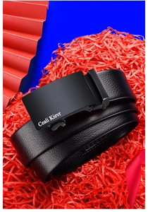 Detail of black lychee grain leather belt with matte metal automatic buckle on red gift fill