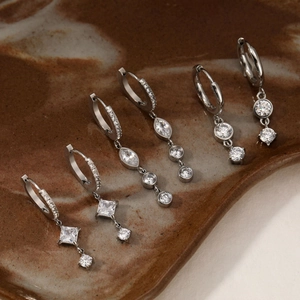 Silver stainless steel earrings with cubic zirconia charms on a brown ceramic plate