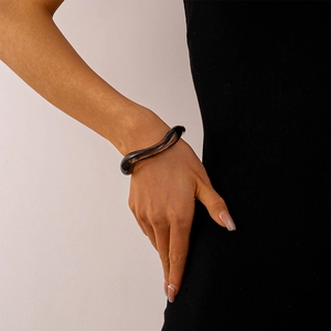 Detail of a dark grey translucent acrylic cuff bracelet with an irregular wave design