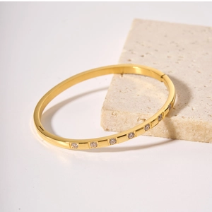 Detail shot of a gold-plated titanium bracelet with white zircons on a beige textured stone
