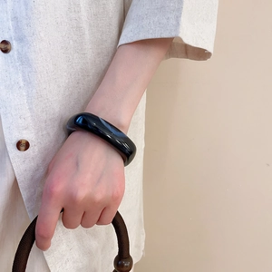 Close-up of a wide polished black acrylic bangle on a model wearing a linen shirt
