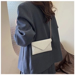 Modische silberne Metallic-Umschlag-Clutch mit Kette auf grauem Blazer getragen